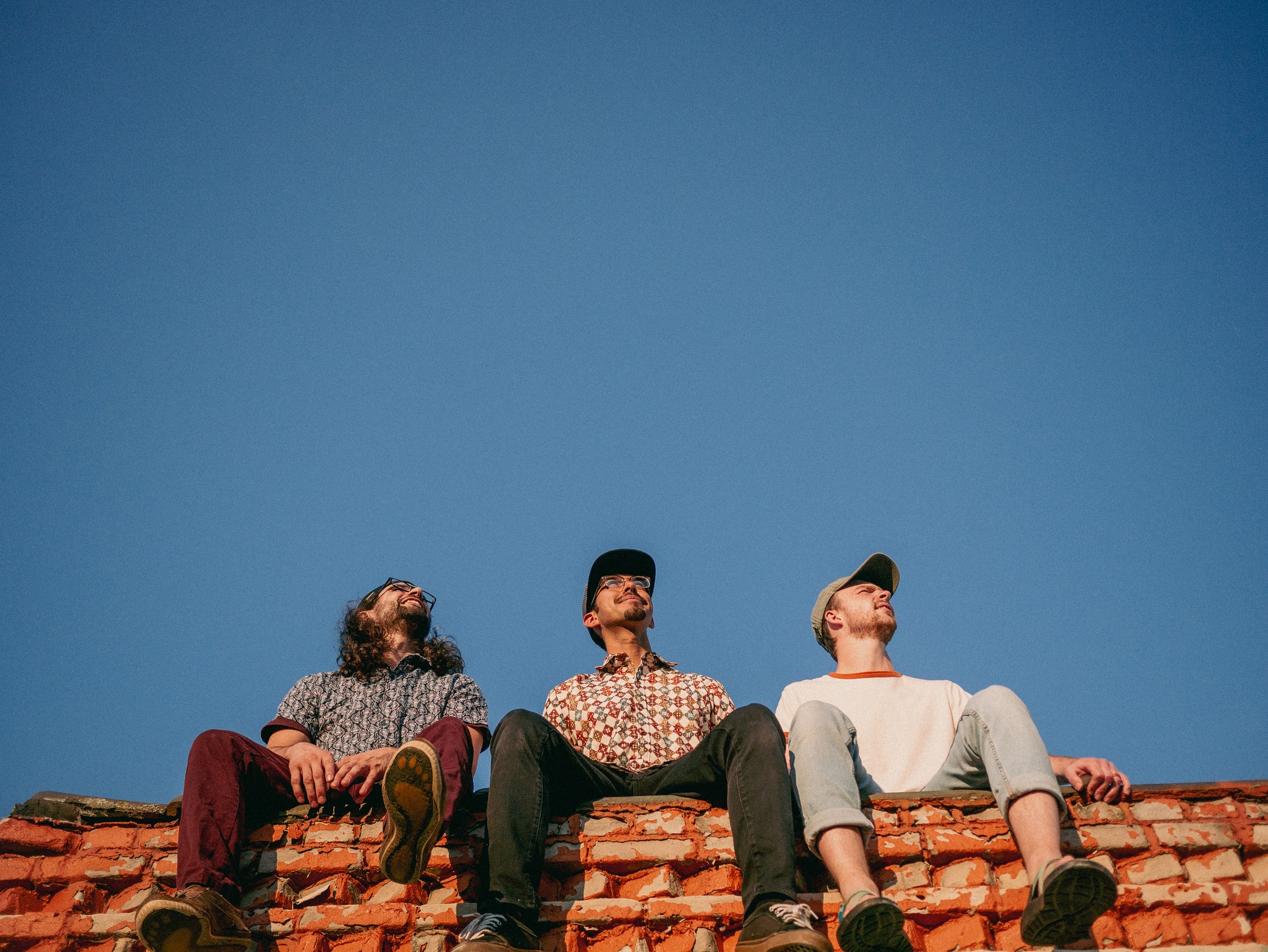 Band members sit on a red tile roof, with clear blue sky above them