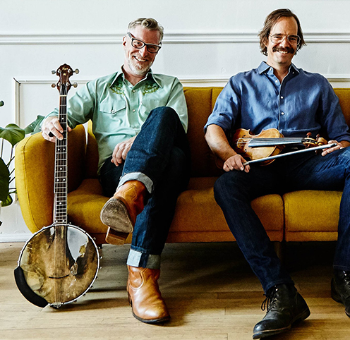 Showman and Coole are pictured on a yellow couch, holding thier instruments