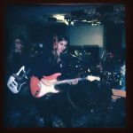 La La Delivery plays on stage in a grainy super-imposed image