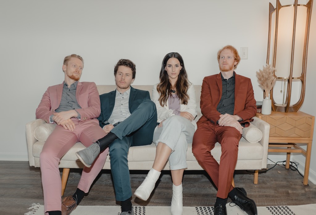 The band is pictured wearing vintage clothes on a couch.